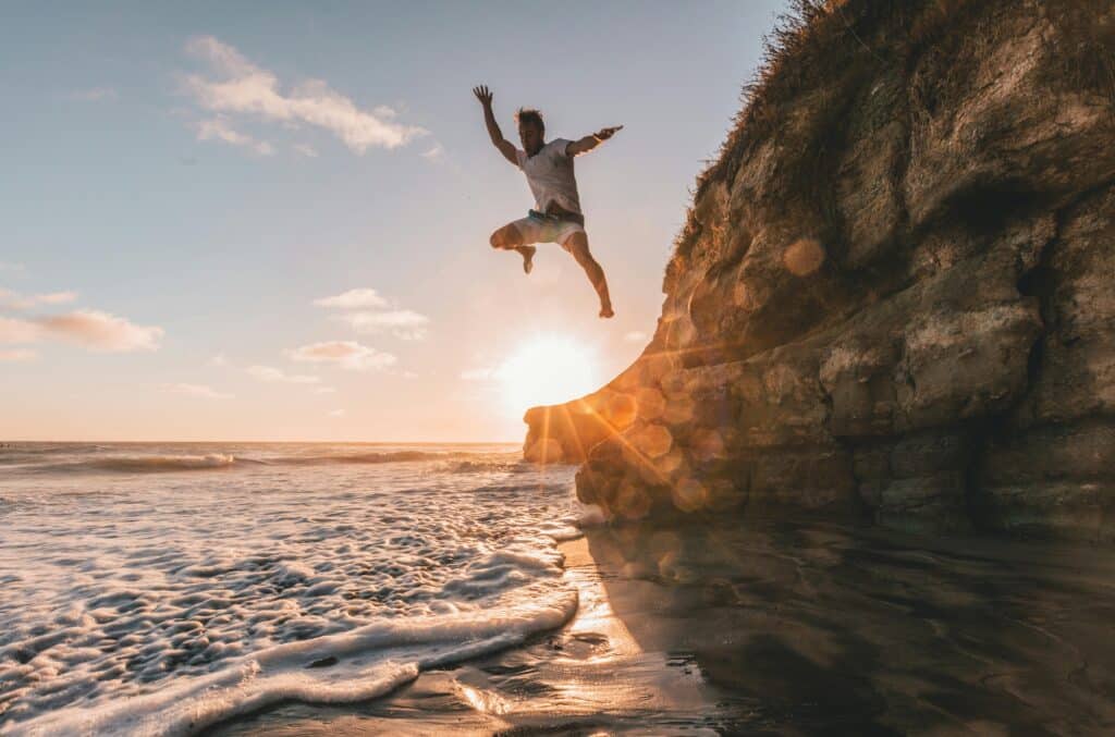 Person jumping near ocean sunset
